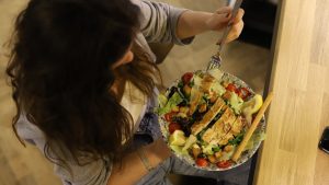 Overhead view of a woman eating a chicken salad balancing health with deliciousness.